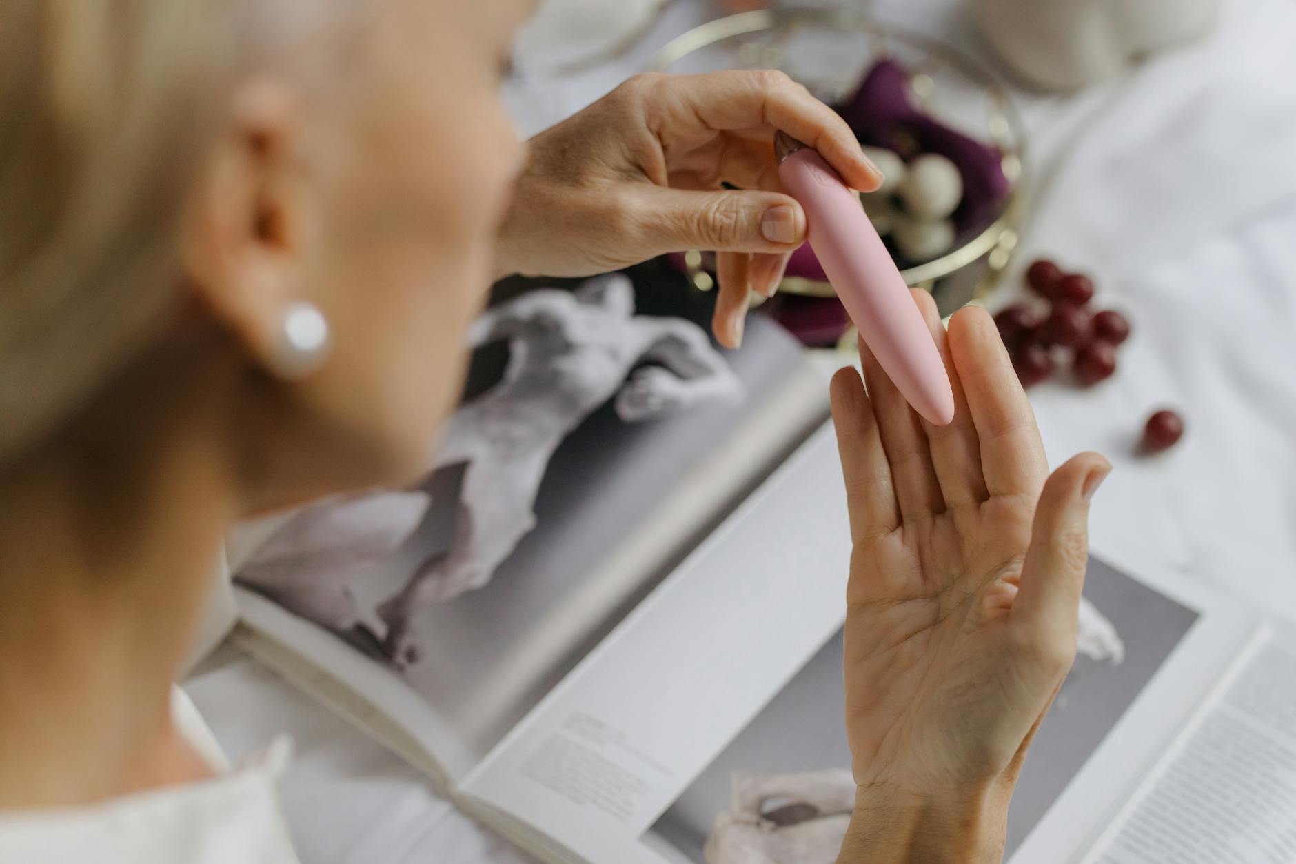 A woman holding a pink vibrator with books in the background, symbolizing intimate exploration and relationship growth.