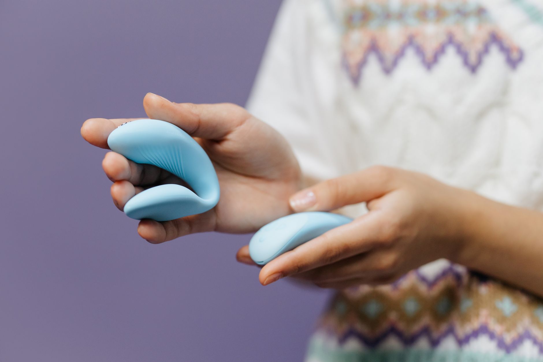 Intimate close-up of hands holding a sleek vibrator against a purple background