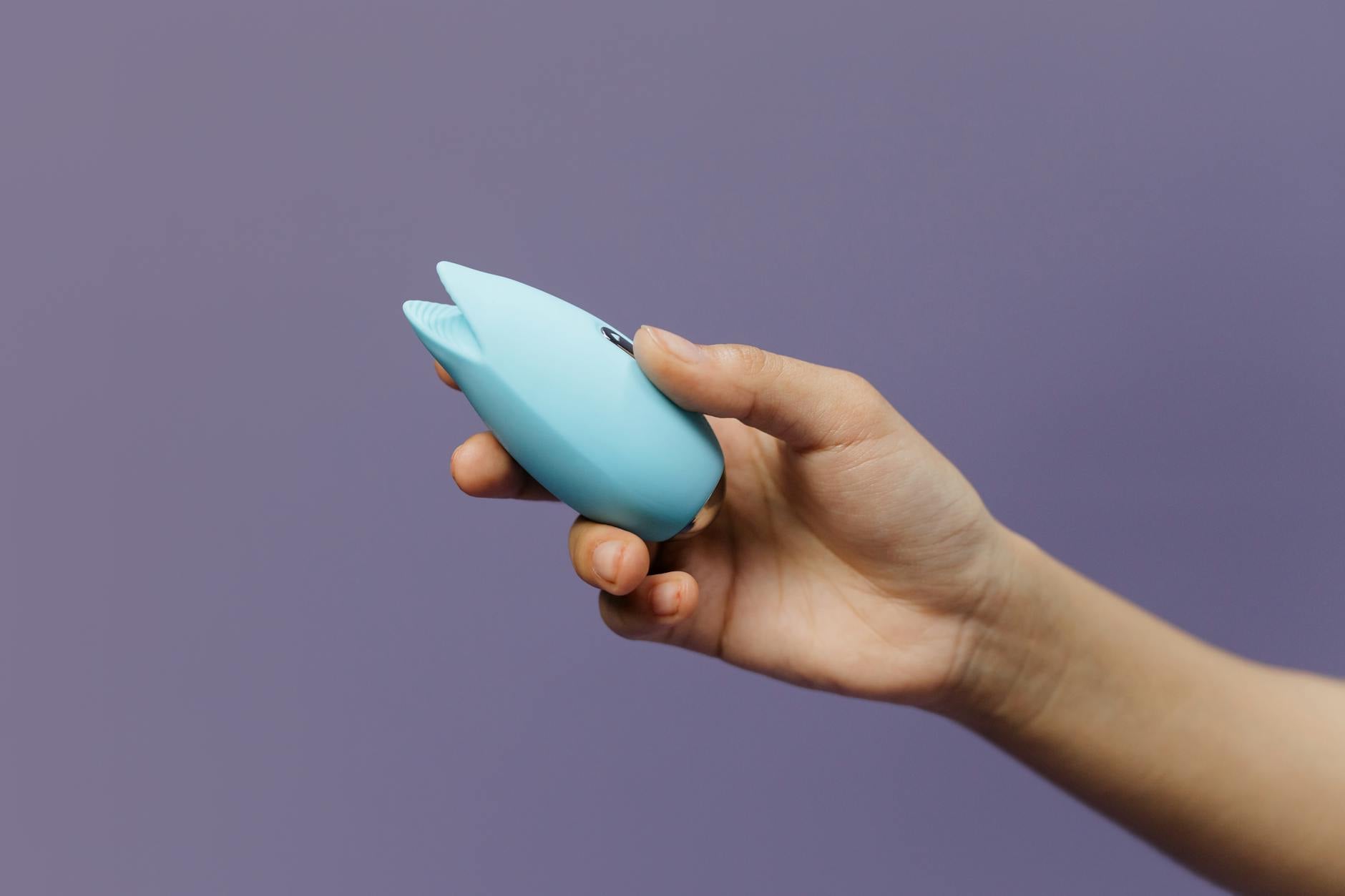 Ein blausilikon Vibrator wird in der Hand gehalten vor lila Hintergrund