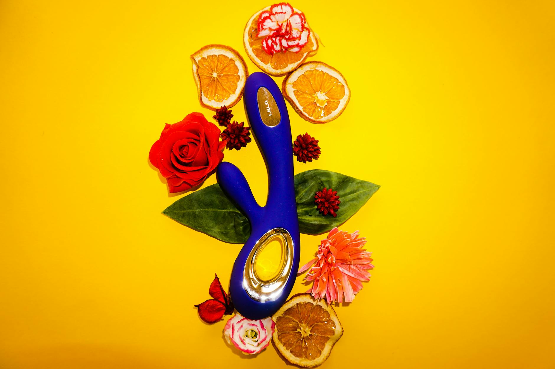 A blue silicone vibrator surrounded by flowers on a yellow background, symbolizing sensual renewal.